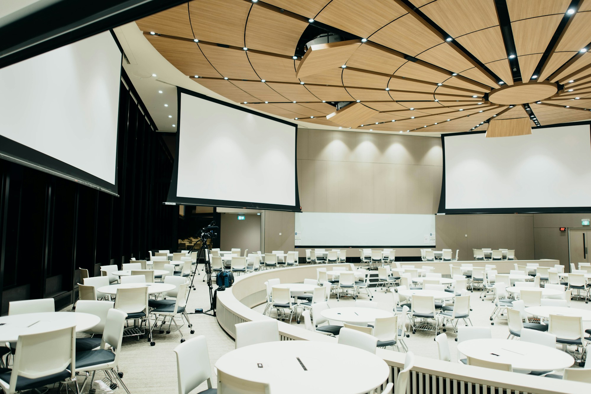 A modern conference venue with screens, round tables, and a production camera